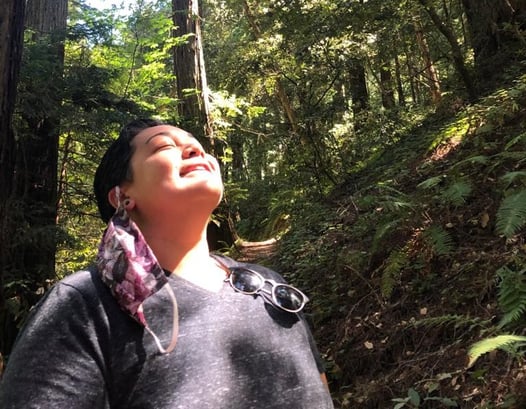 Person smiling and looking up at sun in forest