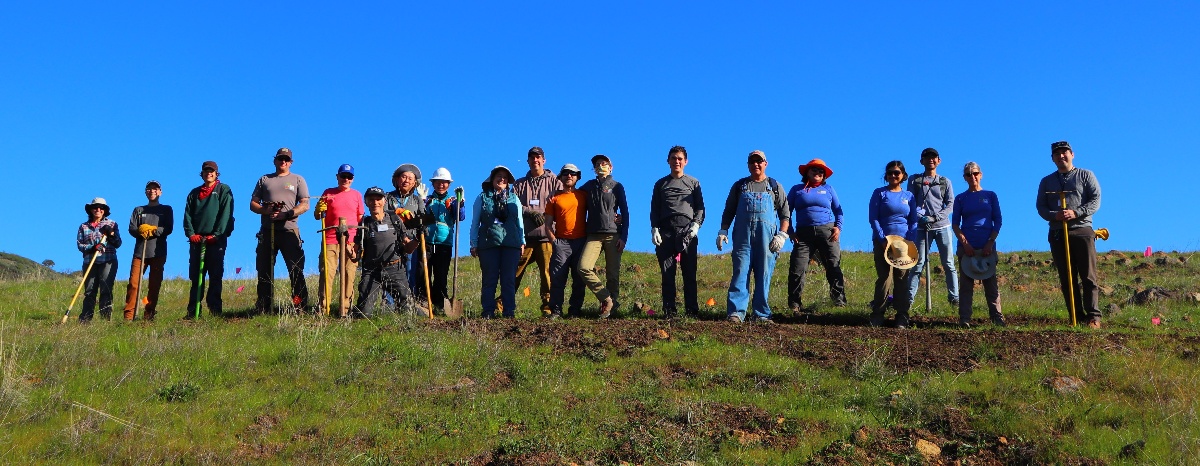 19 volunteers and staff stand in a rowon a hillside smiling at the camera.