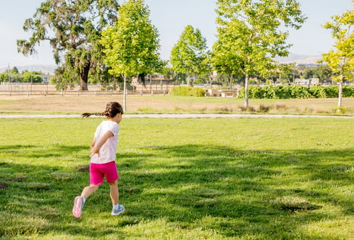 Child running across green field at park