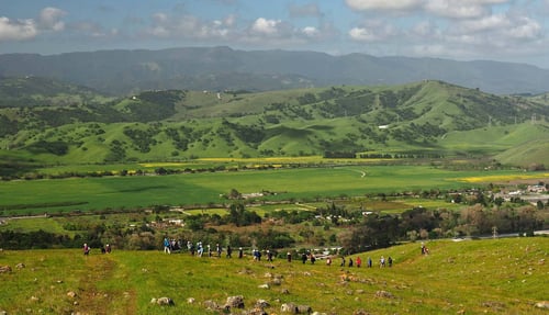 A group of hikers walks along a ridgeline, with green Coyote Valley below them